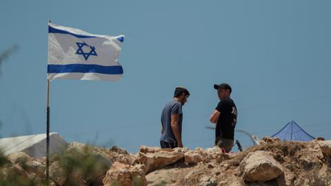 Zwei Männer stehen neben einer israelischen Flagge, die im Wind flattert.