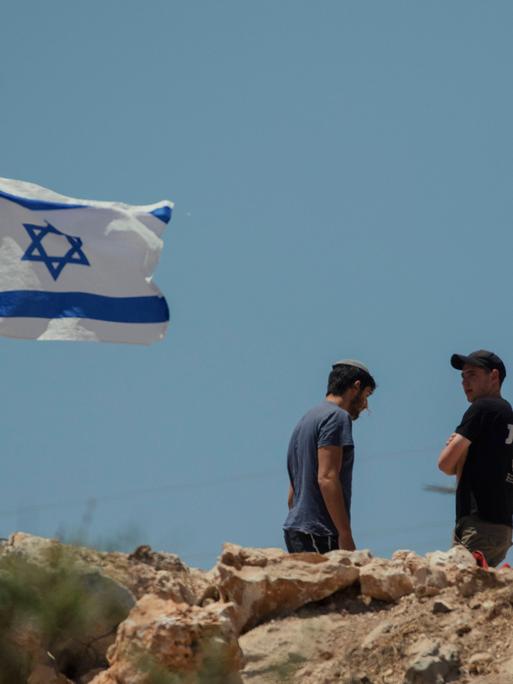 Zwei Männer stehen neben einer israelischen Flagge, die im Wind flattert.