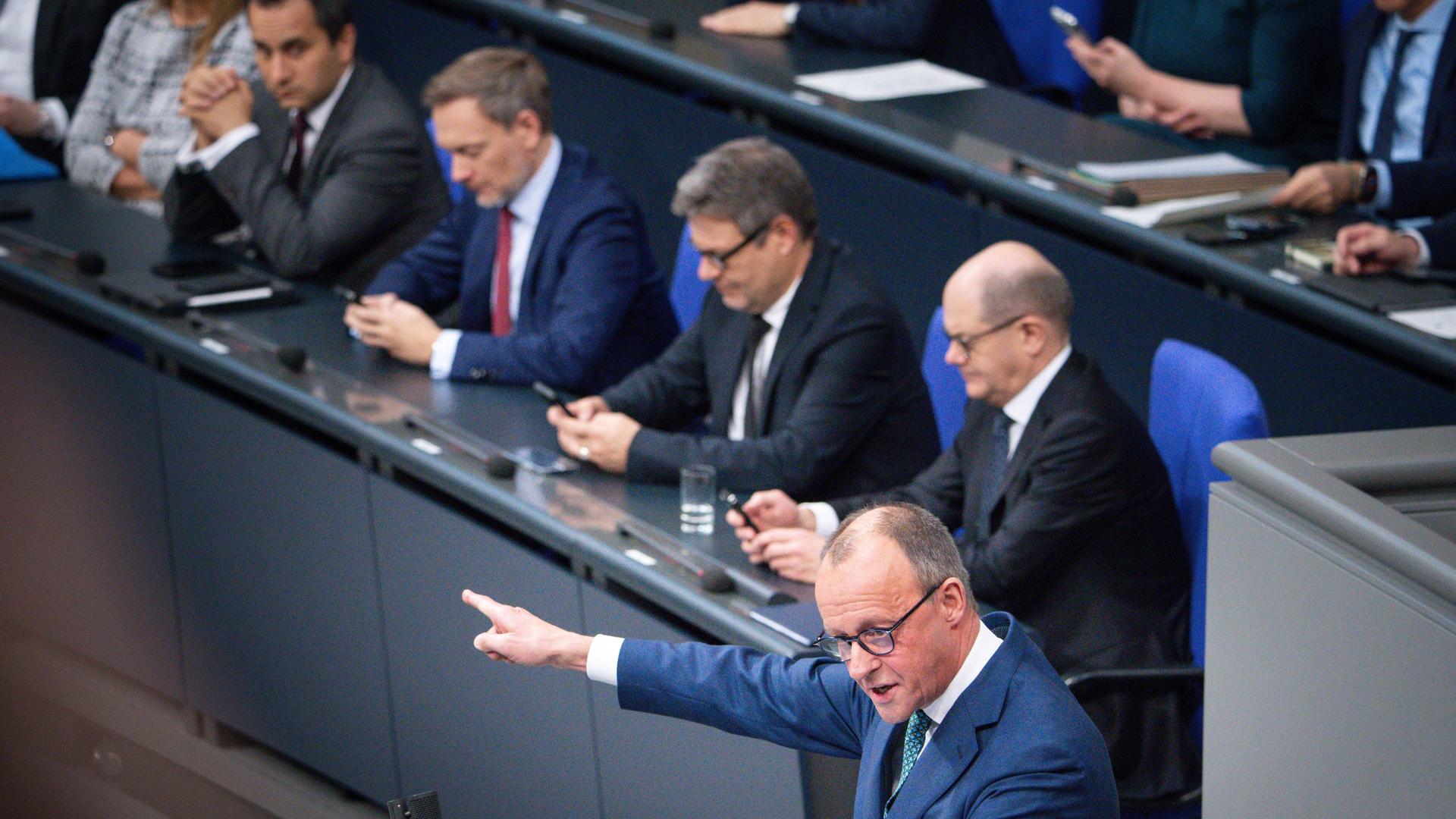 CDU-Politiker Friedrich Merz hält im Bundestag eine Rede, mit Bundeskanzler Olaf Scholz, Bundeswirtschaftsminister Robert Habeck und Finanzminister Christian Lindner im Hintergrund.