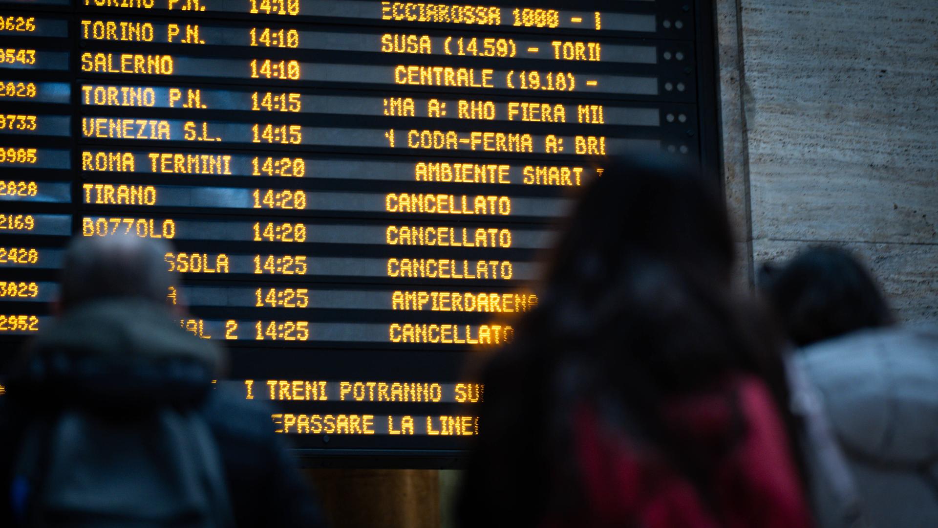 Reisende betrachten eine Informationstafel an einem Bahnhof. Darauf stehen ausgefallene Zugverbindungen. Reisende betrachten eine Informationstafel an einem Bahnhof. Darauf stehen ausgefallene Zugverbindungen.