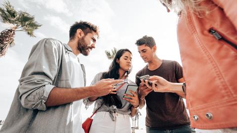 Ein paar junge Leute stehen im Kreis und halten ihre Smartphones in der Hand. Sie diskutieren angeregt miteinander.