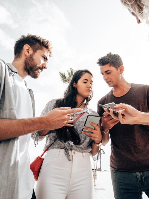 Ein paar junge Leute stehen im Kreis und halten ihre Smartphones in der Hand. Sie diskutieren angeregt miteinander.