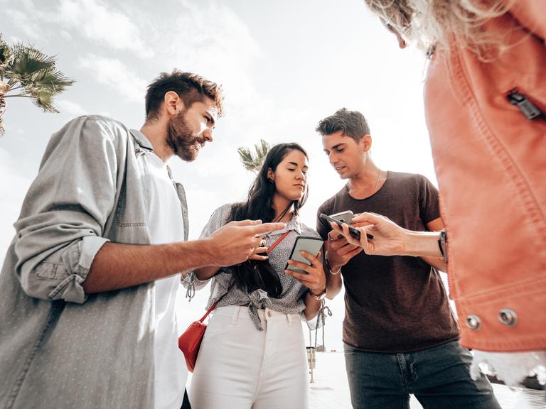 Ein paar junge Leute stehen im Kreis und halten ihre Smartphones in der Hand. Sie diskutieren angeregt miteinander.