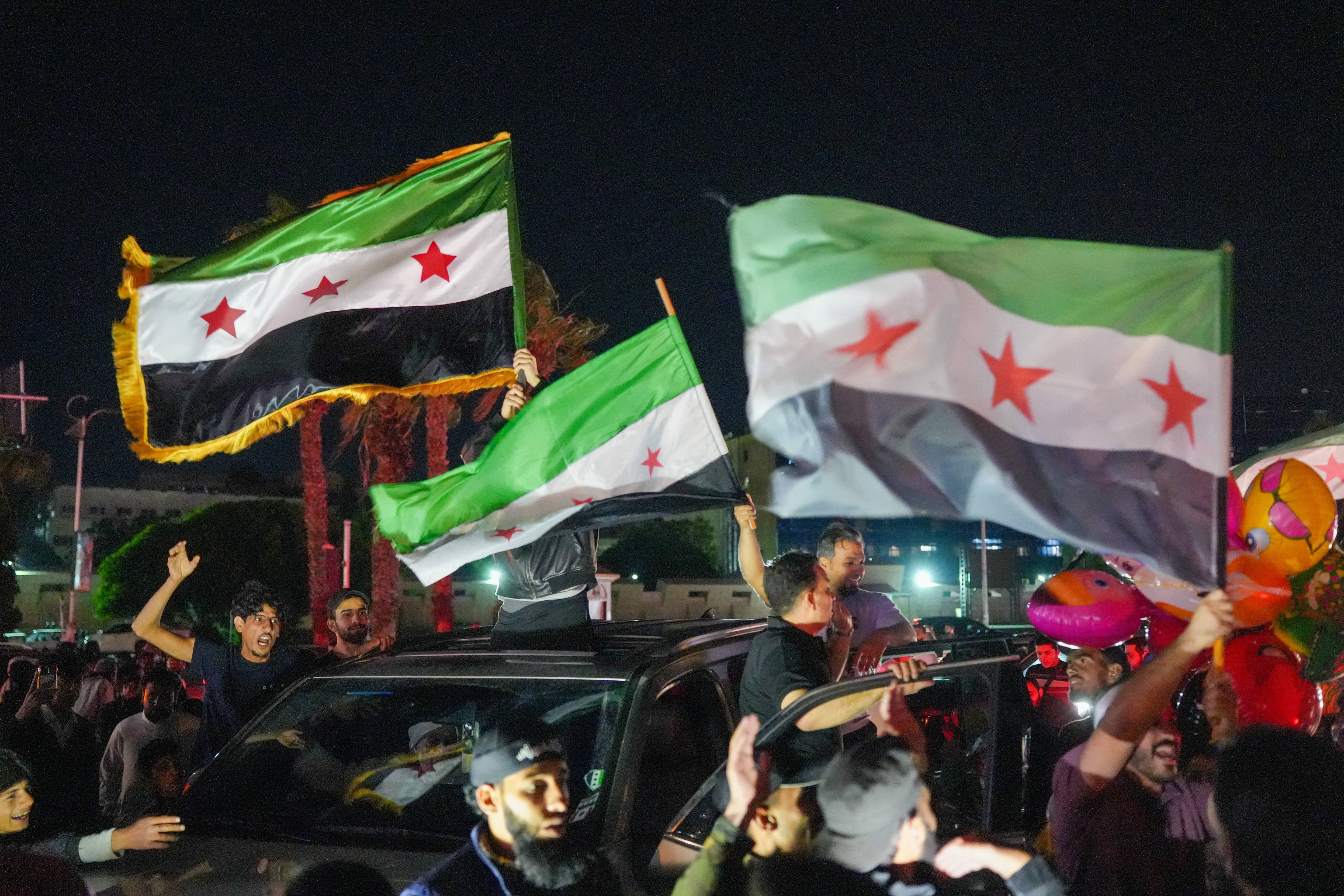 Feiernde schwenken nachts aus einem fahrenden Auto syrische Fahnen.