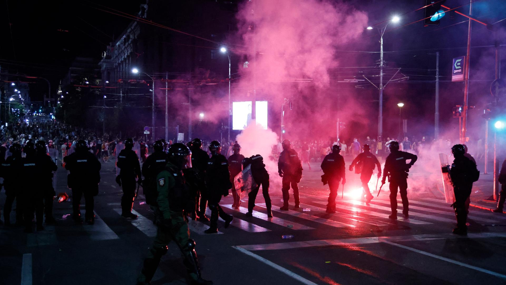 Auf einer nächtlichen Kreuzung in Belgrad stehen sich uniformierte Polizisten und Demonstranten gegenüber.