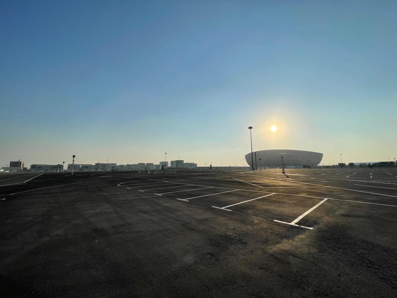 Man sieht eine Aufnahme mit dem Lusail-Stadion im Sonnenuntergang, umgeben von einem gigantischen, leeren Parkplatz.