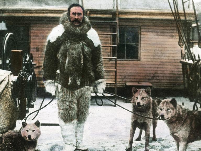 Eine kolorierte historische Fotografie des Polarforschers Robert Ewin Peary, der behauptete, 1909 den Nordpol entdeckt zu haben. Er trägt dicke Fellkleidung und hält mehrere Polarhunde an der Leine.