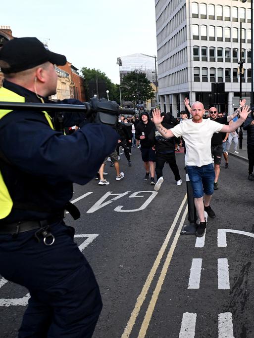 Weiße männliche Demonstranten stehen auf einer Straße Polizisten in Riot-Gear gegenüber.