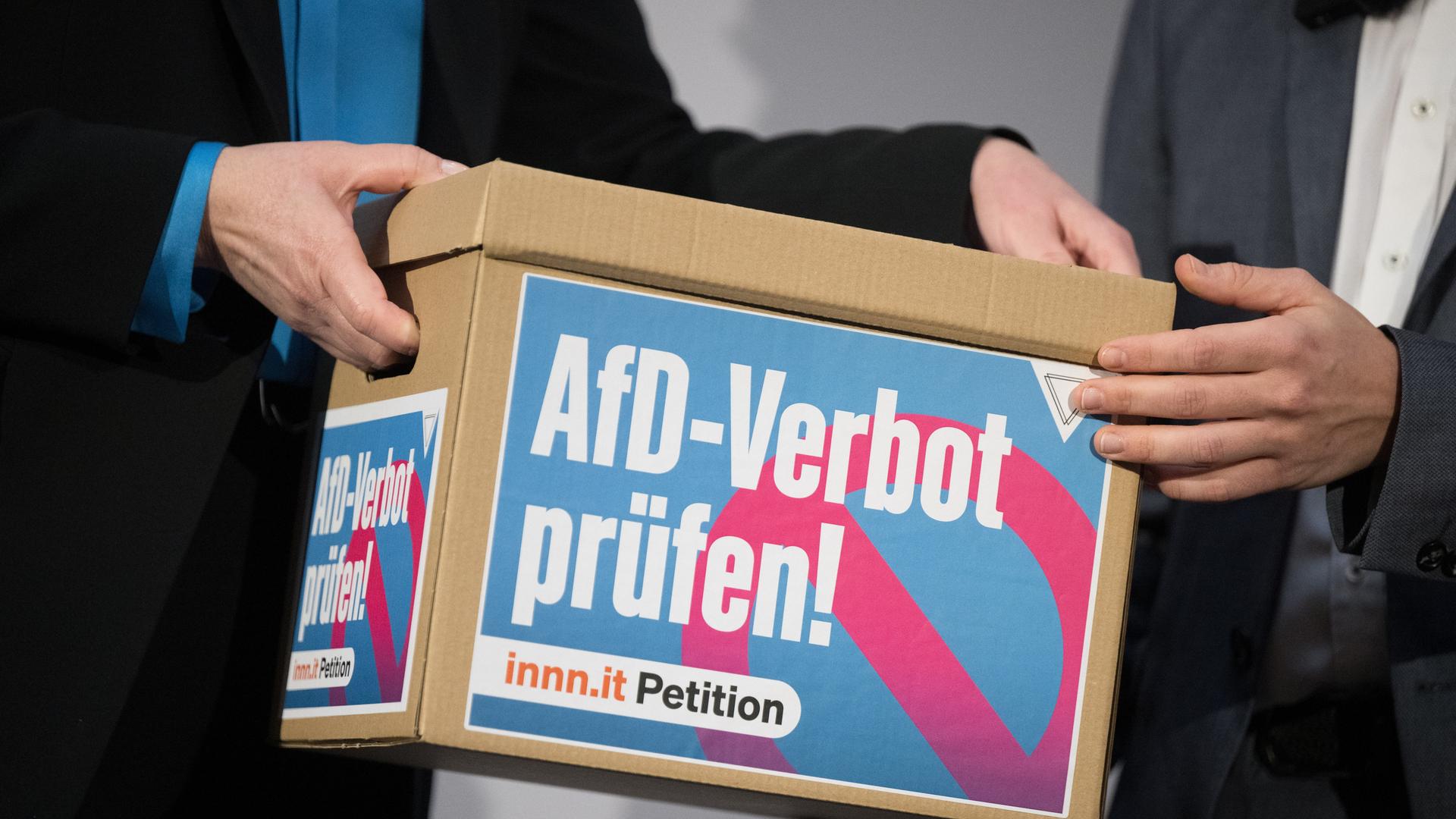 Ein Händepaar übergibt einen Karton mit Unterschriften der Petition "AfD-Verbot prüfen!" an ein anderes.