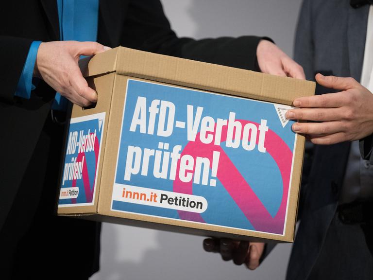Ein Händepaar übergibt einen Karton mit Unterschriften der Petition "AfD-Verbot prüfen!" an ein anderes. Ein Händepaar übergibt einen Karton mit Unterschriften der Petition "AfD-Verbot prüfen!" an ein anderes.