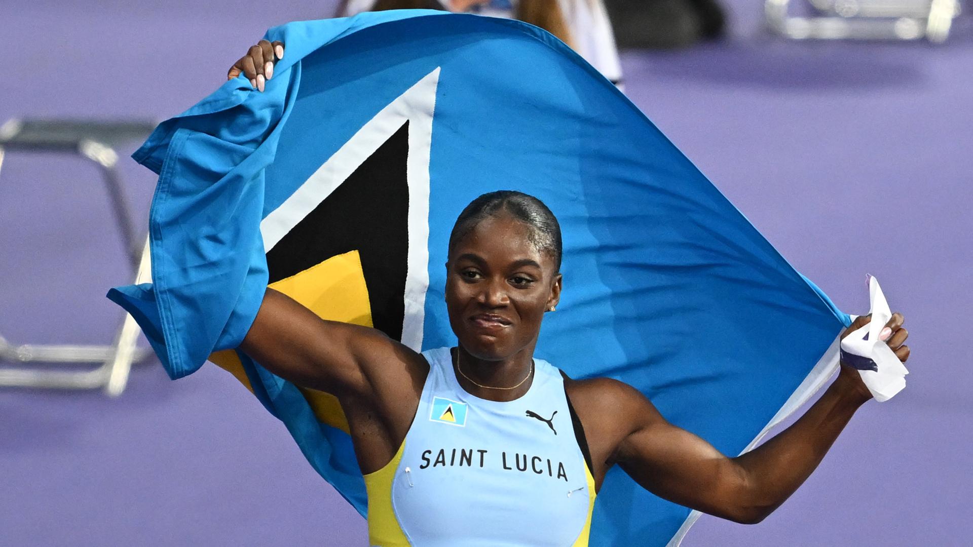 Die Sprinterin Julien Alfred aus St. Lucia jubelt nach dem 100-Meter-Rennen von Paris. Hinter ihrem Rücken hält sie die Fahne ihres Heimatlands. 