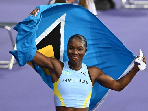 Die Sprinterin Julien Alfred aus St. Lucia jubelt nach dem 100-Meter-Rennen von Paris. Hinter ihrem Rücken hält sie die Fahne ihres Heimatlands. 