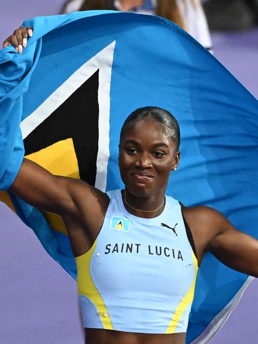 Die Sprinterin Julien Alfred aus St. Lucia jubelt nach dem 100-Meter-Rennen von Paris. Hinter ihrem Rücken hält sie die Fahne ihres Heimatlands. 