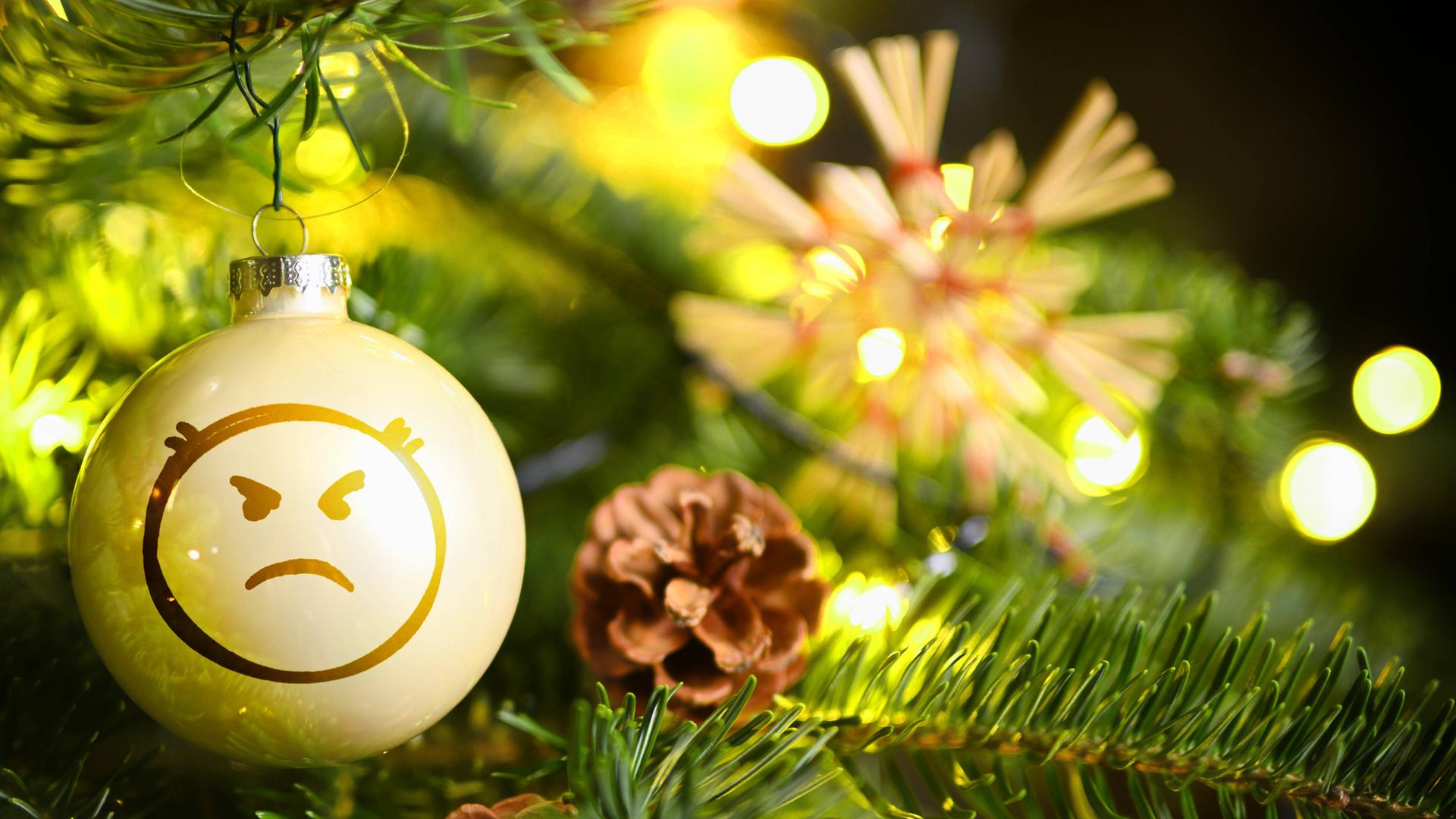 Weihnachtskugel mit Wut-Emoji hängt an einem Weihnachtsbaum.