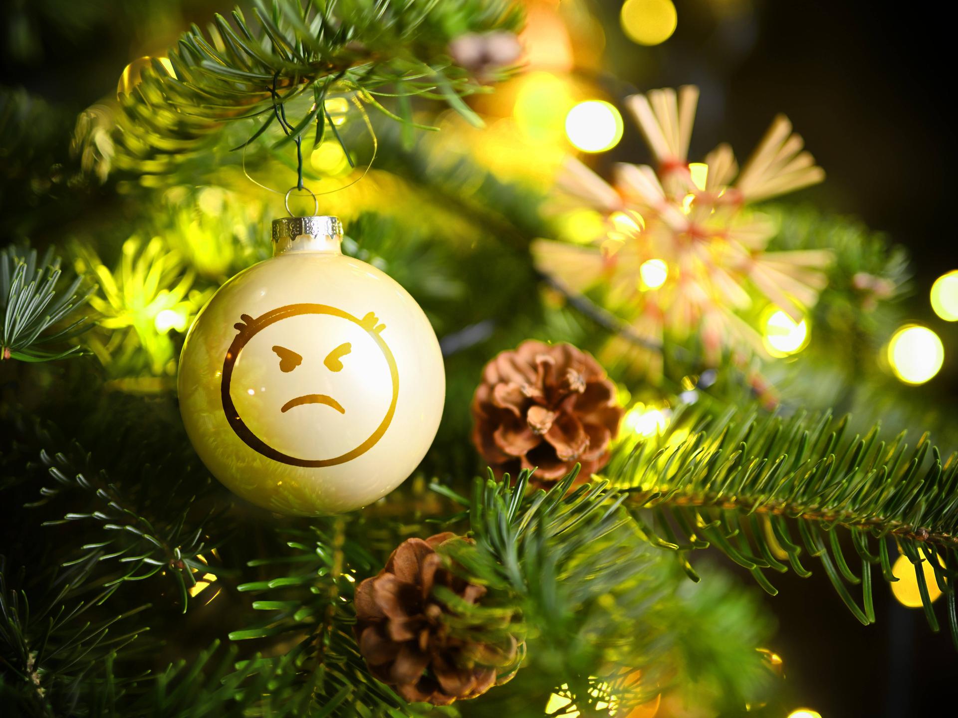 Weihnachtskugel mit Wut-Emoji hängt an einem Weihnachtsbaum.