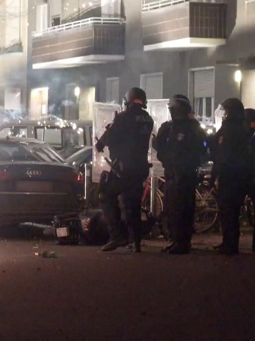 Polizeibeamte stehen hinter explodierendem Feuerwerk in Berlin Neukölln