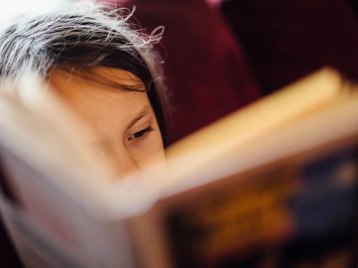 Fotografie eines aufgeschlagenen Buches, das ein Kind in den Händen hält und darin liest.