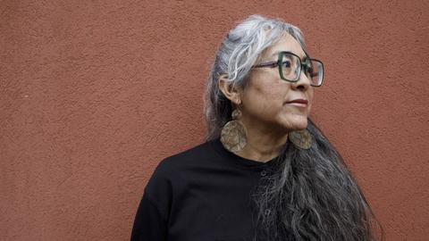 Cristina Rivera Garza steht vor einer ockerfarbenen Wand und schaut zur Seite.