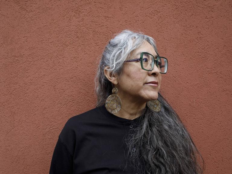 Cristina Rivera Garza steht vor einer ockerfarbenen Wand und schaut zur Seite.