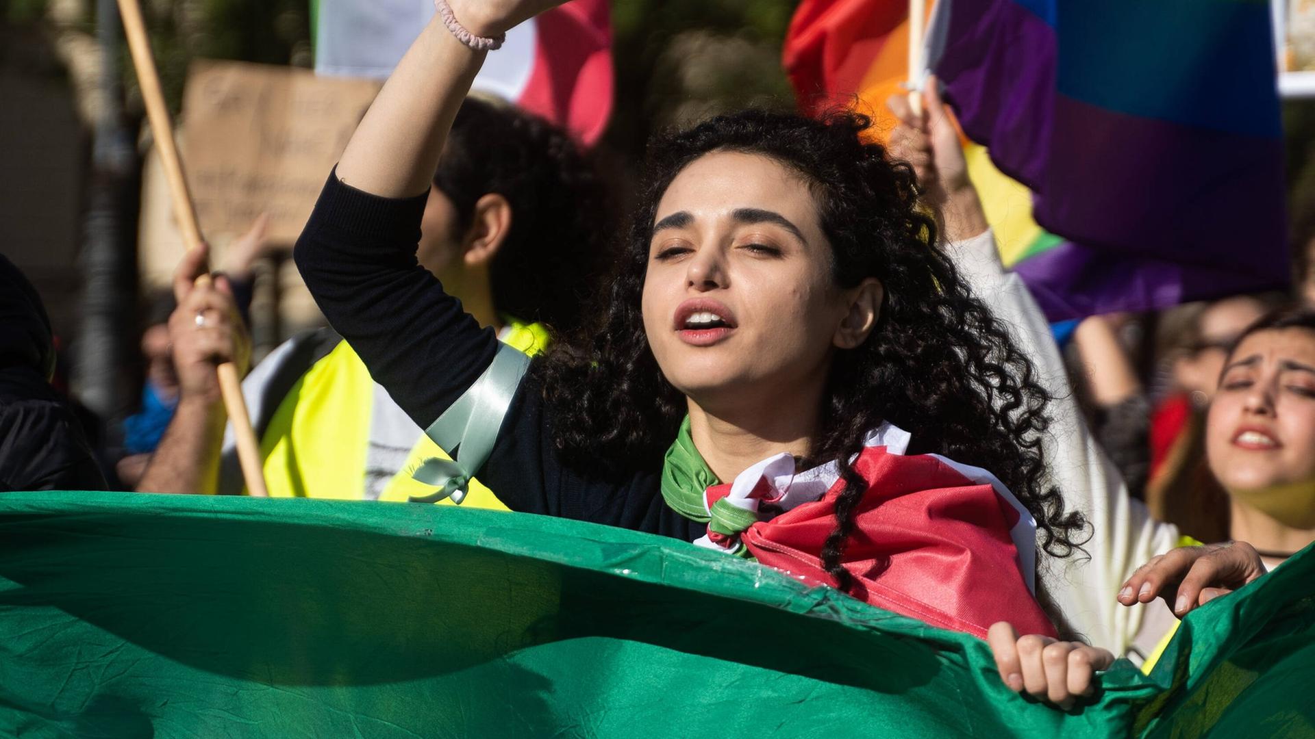 Protest für Mahsa Amini in München. Eine Teilnehmerin macht ein Peace Symbol. Im Vordergrund ist die Flagge des Iran zu sehen.