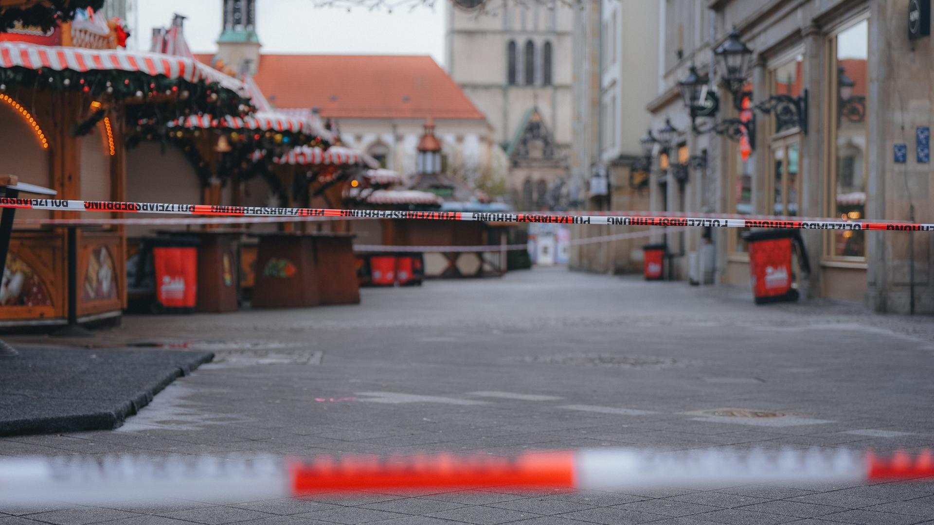 Eine Polizeiabsprerrung mit zwei rot-weißen Bändern vor geschlossenen Ständen auf dem Magdeburger Weihnachtsmarkt. Im Hintergrund zeichen sich Teile der Johanniskirche ab.