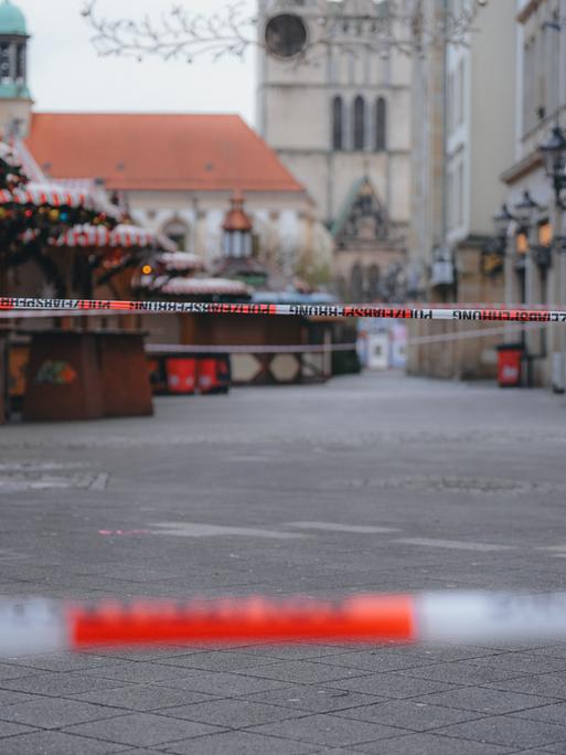 Eine Polizeiabsprerrung mit zwei rot-weißen Bändern vor geschlossenen Ständen auf dem Magdeburger Weihnachtsmarkt. Im Hintergrund zeichen sich Teile der Johanniskirche ab.