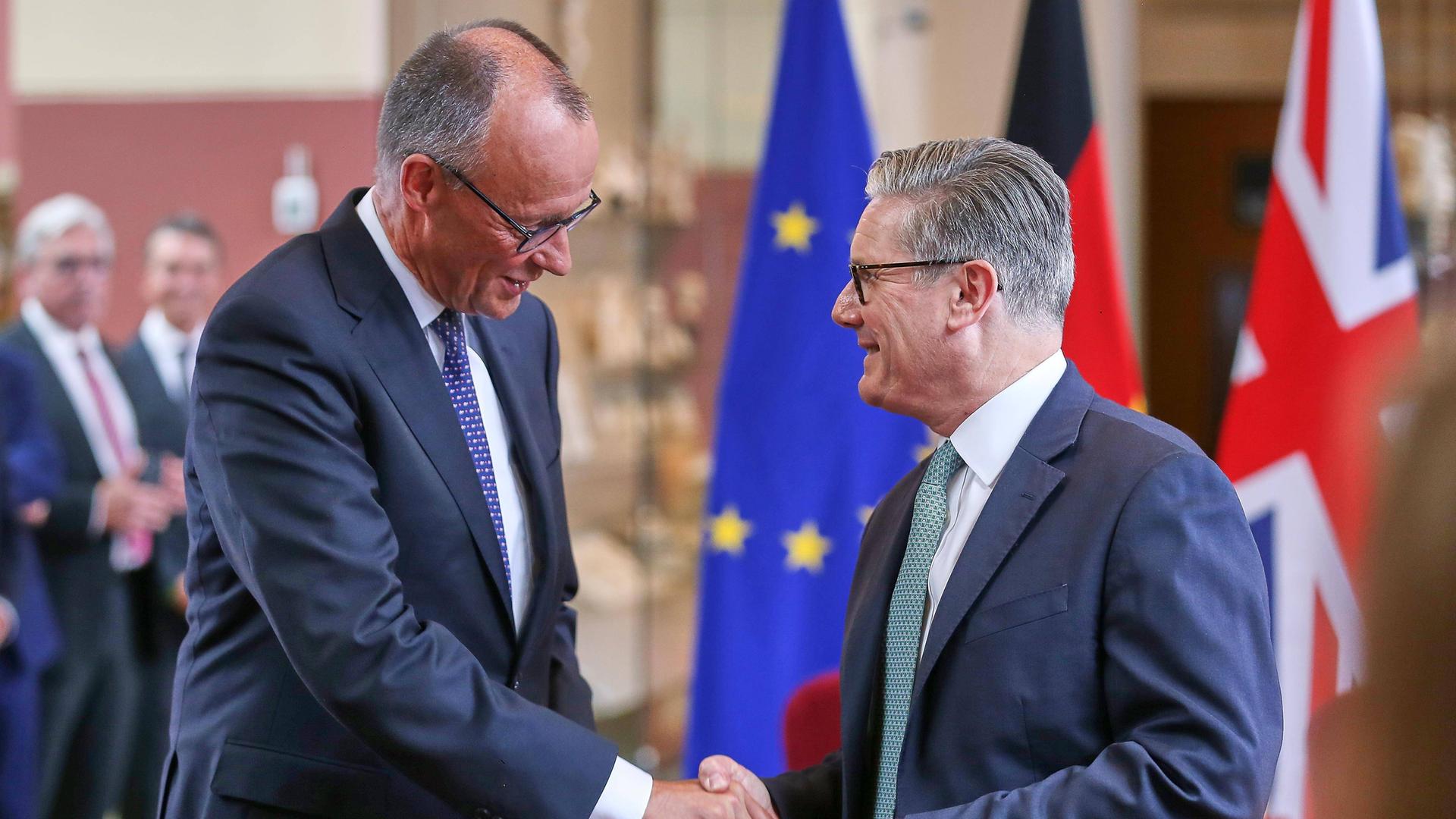 Bundeskanzler Friedrich Merz und Großbritanniens Premier Keir Starmer geben sich im Rahmen der Unterzeichnung vor Flaggen die Hand