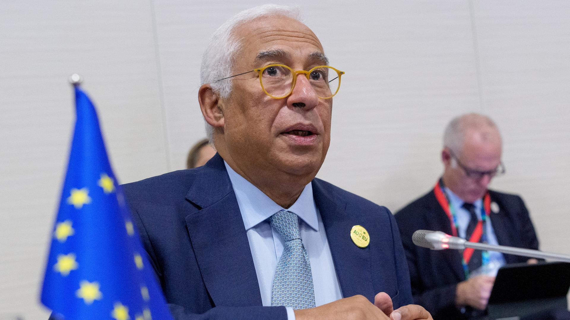 António Costa sitzt an einem Konferenztisch und spricht in ein Mikrofon. Vor ihm steht die Flagge der EU.