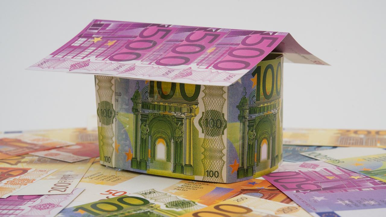 Ein Haus aus künstlichen Geldscheinen steht  auf weiteren Geldscheinen