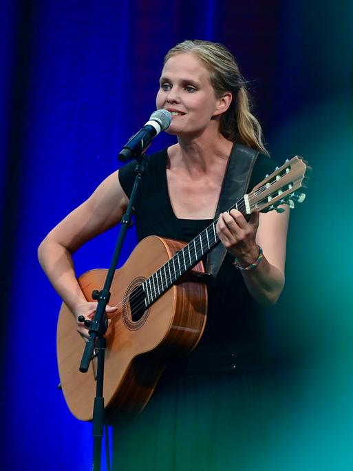 Dota Kehr, Sängerin und Liedermacherin, ist bei ihrem Konzert auf der Bühne des Sommerprogramms der Stiftung Schloss Neuhardenberg zu sehen. Sie singt in ein Mikrophon und spielt die Gitarre.