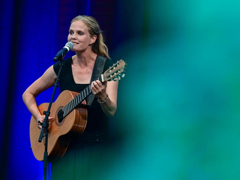 Dota Kehr, Sängerin und Liedermacherin, ist bei ihrem Konzert auf der Bühne des Sommerprogramms der Stiftung Schloss Neuhardenberg zu sehen. Sie singt in ein Mikrophon und spielt die Gitarre.