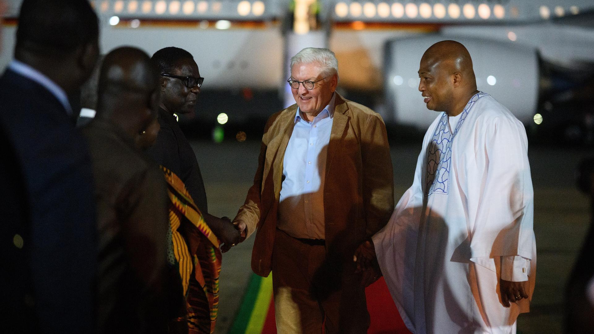 Bundespräsident Steinmeier steht vor dem Regierungsflieger am Flughafen. Ihm gegenüber stehen mehrere Männer. Neben ihm steht der Außenminister von Ghana, Ablakwa. Es ist dunkel.