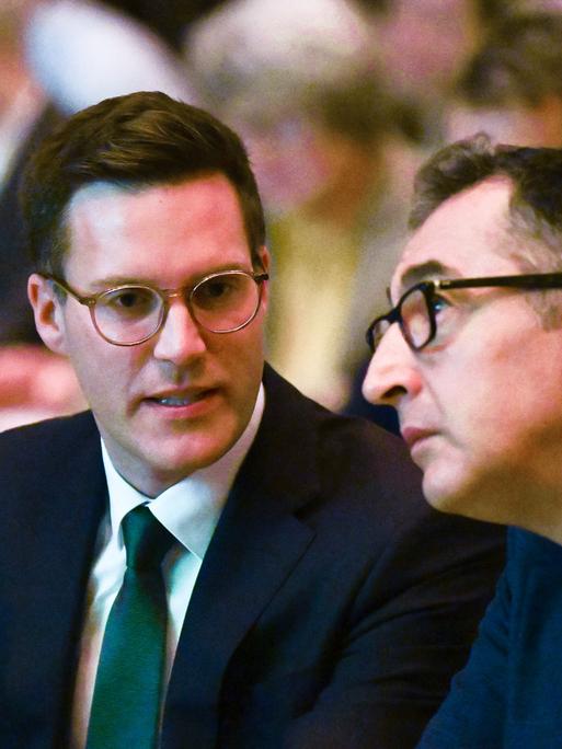 Manuel Hagel (l, CDU) und Cem Özdemir (r, Bündnis 90 / Die Grünen) sitzen nebeneinander bei einer Veranstaltung. Ihre Köpfe sind einander zugeneigt, sie scheinen im Gespräch.