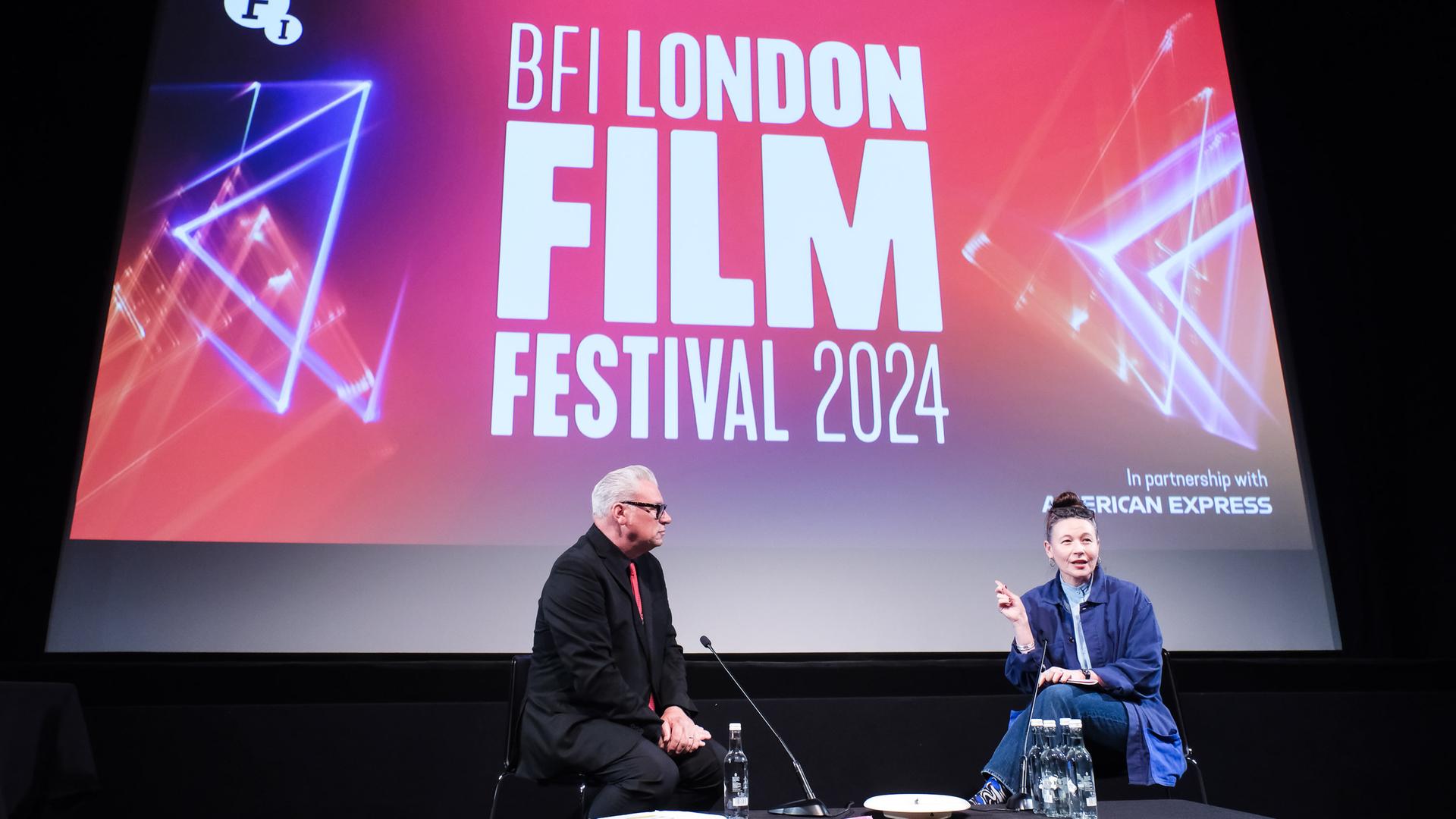 Die Direktorin des LFF, Kristy Matheson, im Gespräch mit dem britischen Filmkritiker Mark Kermode auf einer Bühne unter einem Bildschrim mit der Aufschrift "BFI London Film Festival 2024" 