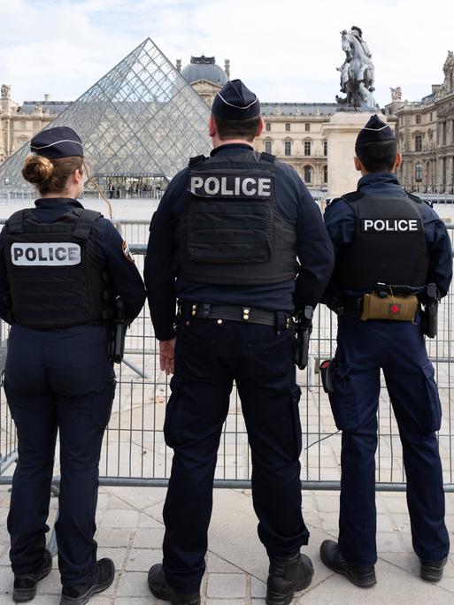 Polizeikräfte vor dem Louvre stehen mit dem Rücken zum Betrachter.