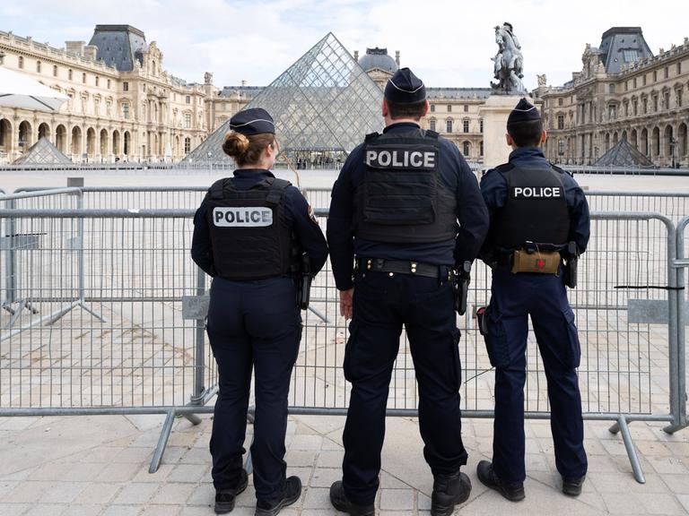 Polizeikräfte vor dem Louvre stehen mit dem Rücken zum Betrachter.