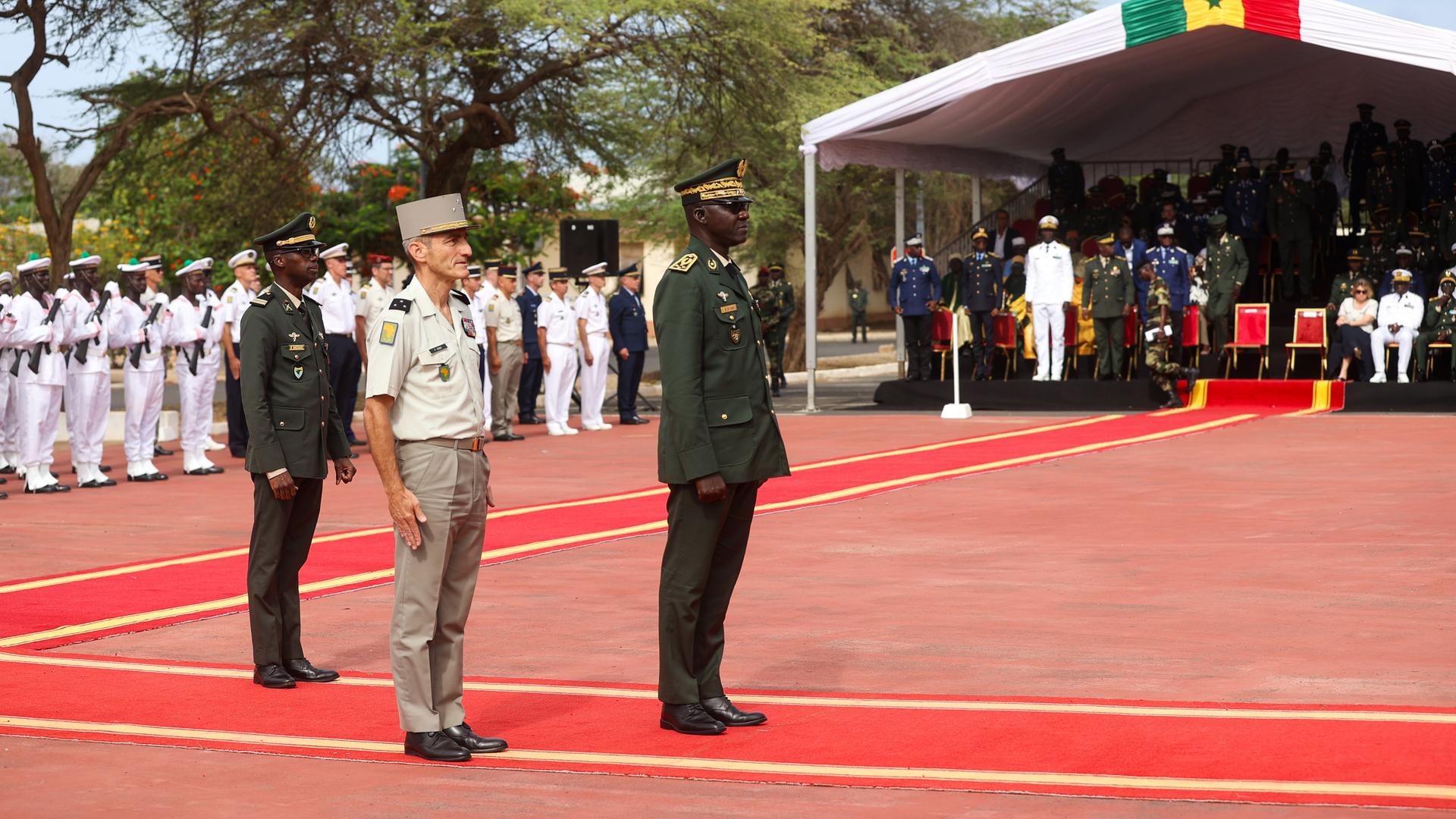 Senegalesische und französische Militärangehörige stehen in Uniformen auf einem roten Platz und nehmen an einer Zeremonie teil.
