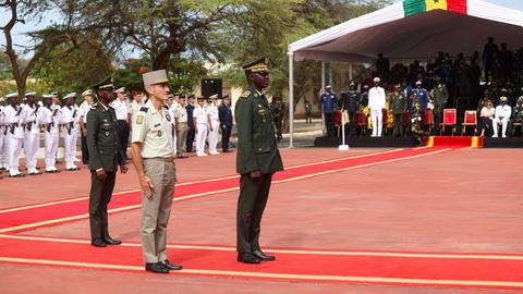 Senegalesische und französische Militärangehörige stehen in Uniformen auf einem roten Platz und nehmen an einer Zeremonie teil.