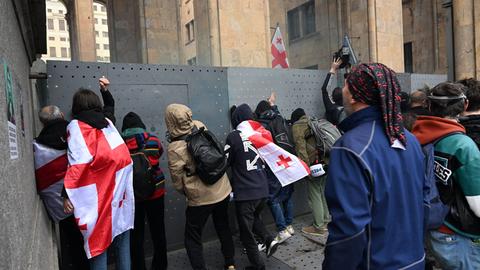 Demonstranten schlagen an eine Absperrung vor dem Parlament in Georgien. Viele tragen georgische Fahnen. 