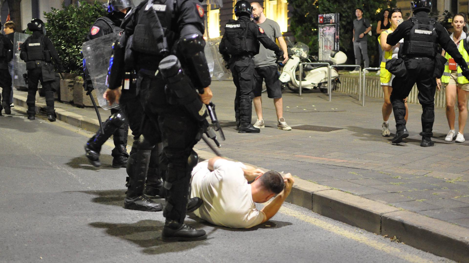 Belgrad am 13. August: Ein junger Mann liegt am Boden, hinter ihm stehen zwei bewaffnete Polizisten