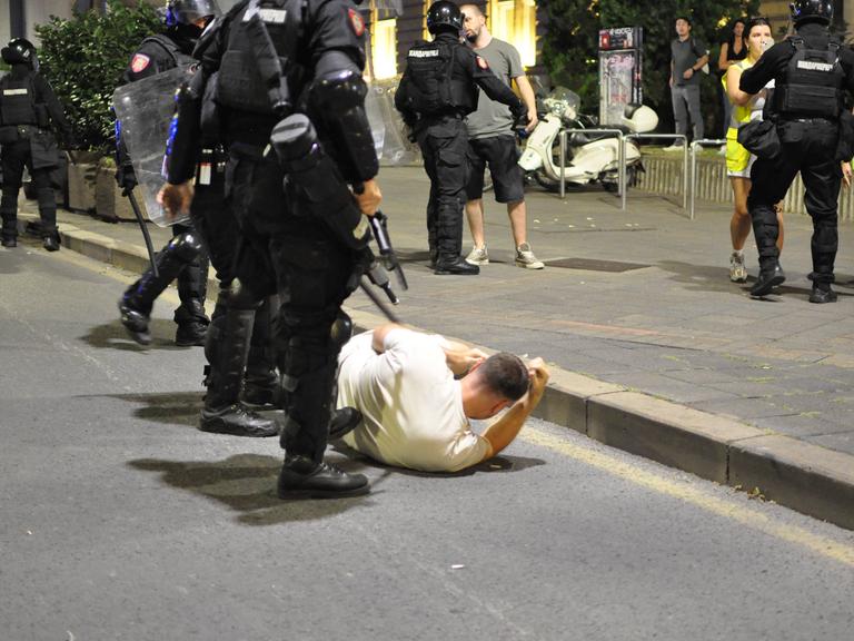 Belgrad am 13. August: Ein junger Mann liegt am Boden, hinter ihm stehen zwei bewaffnete Polizisten
