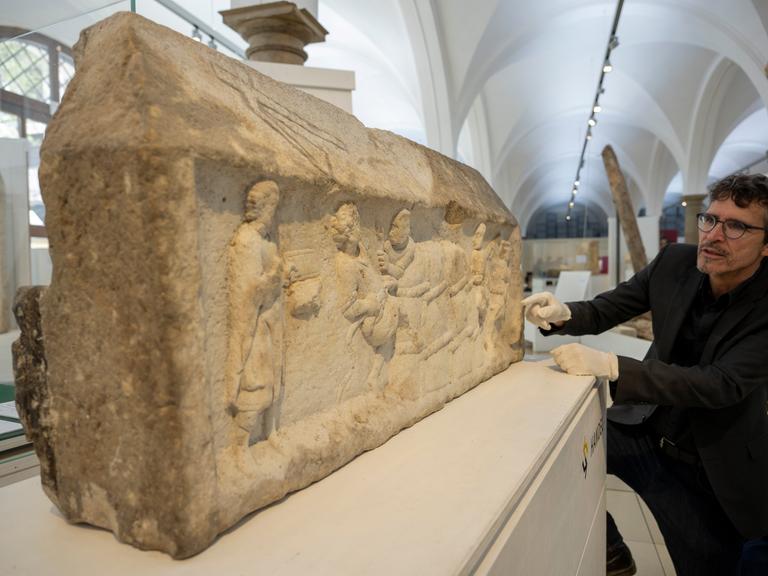 Ein großer Steinblock mit eingemeißelten Figuren: Die Augsburger Grabreliefs zeigen Motive aus dem Wein- und Textilhandel. 