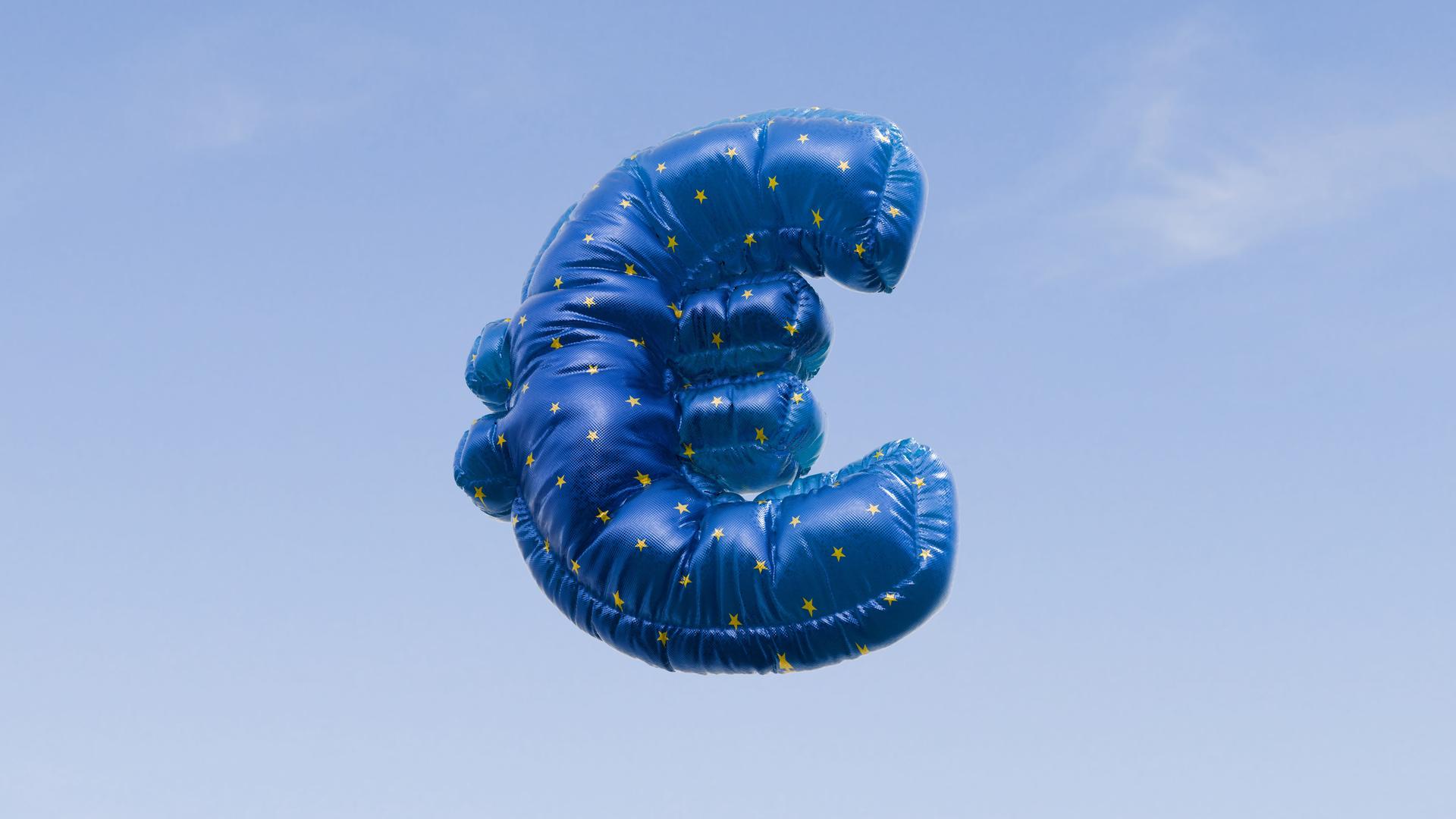 Ein mit Helium gefüllter Ballon in Form des Euro-Symbols schwebt vor einem strahlend blauen Himmel. Ein mit Helium gefüllter Ballon in Form des Euro-Symbols schwebt vor einem strahlend blauen Himmel.