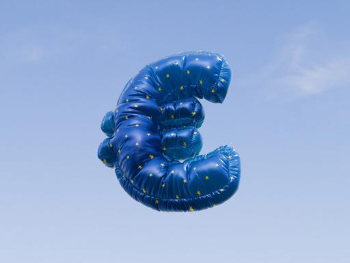 Ein mit Helium gefüllter Ballon in Form des Euro-Symbols schwebt vor einem strahlend blauen Himmel. Ein mit Helium gefüllter Ballon in Form des Euro-Symbols schwebt vor einem strahlend blauen Himmel.