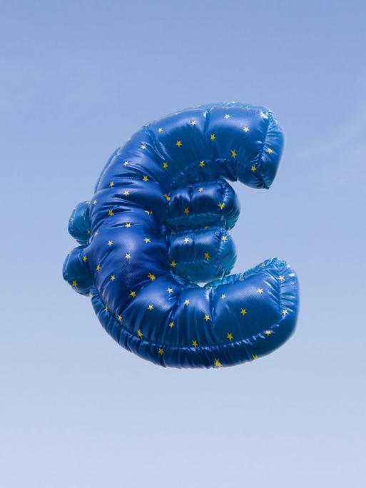 Ein mit Helium gefüllter Ballon in Form des Euro-Symbols schwebt vor einem strahlend blauen Himmel.