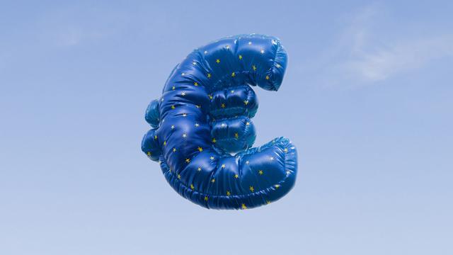 Ein mit Helium gefüllter Ballon in Form des Euro-Symbols schwebt vor einem strahlend blauen Himmel.