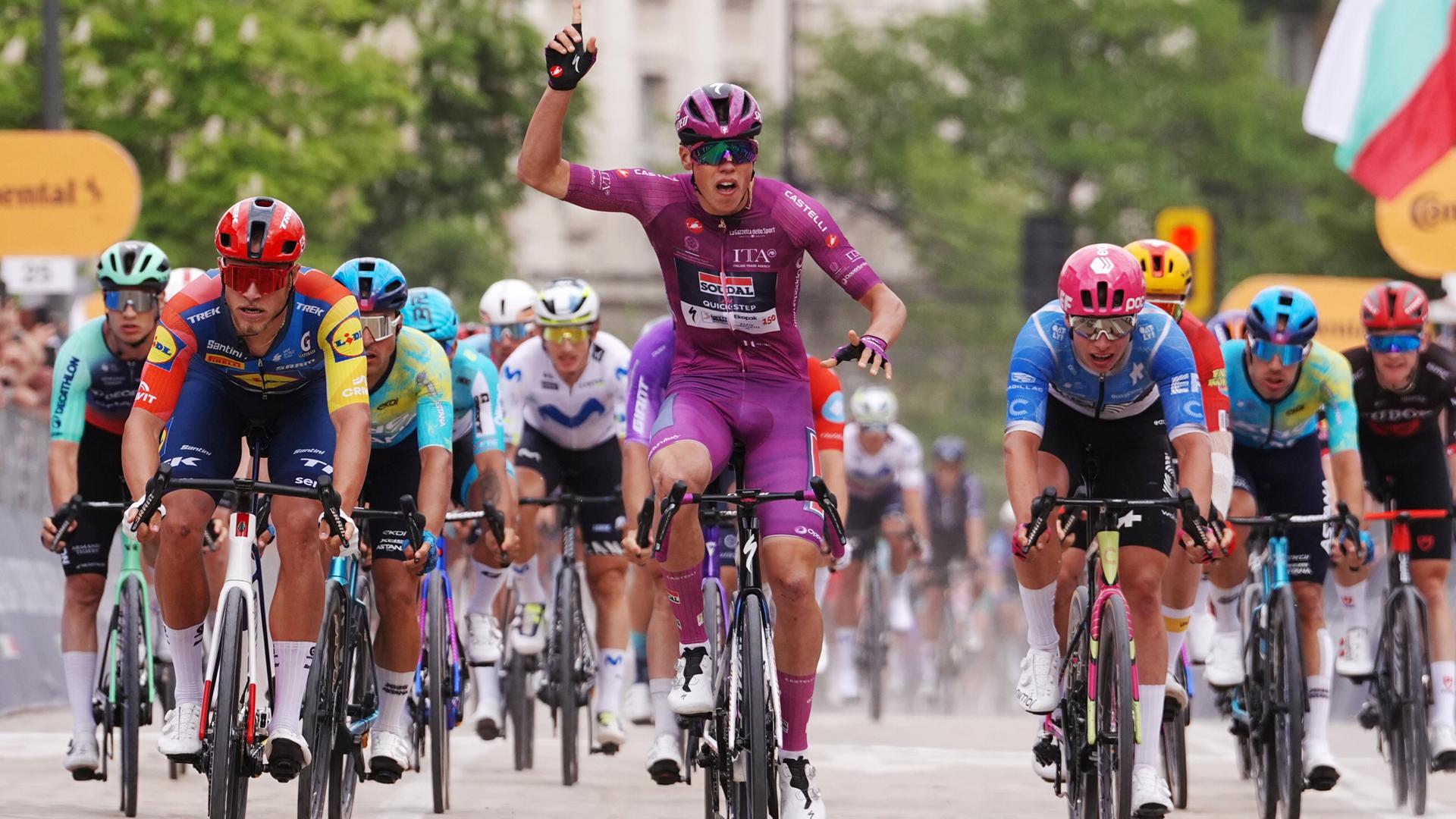 Giro d'Italia: Paul Magnier gewinnt die dritte Etappe. Er streckt den rechten Arm nach oben und freut sich über seinen Sieg; hinter ihm sind zahlreiche andere Radrennfahrer zu sehen. Giro d'Italia: Paul Magnier gewinnt die dritte Etappe. Er streckt den rechten Arm nach oben und freut sich über seinen Sieg; hinter ihm sind zahlreiche andere Radrennfahrer zu sehen.