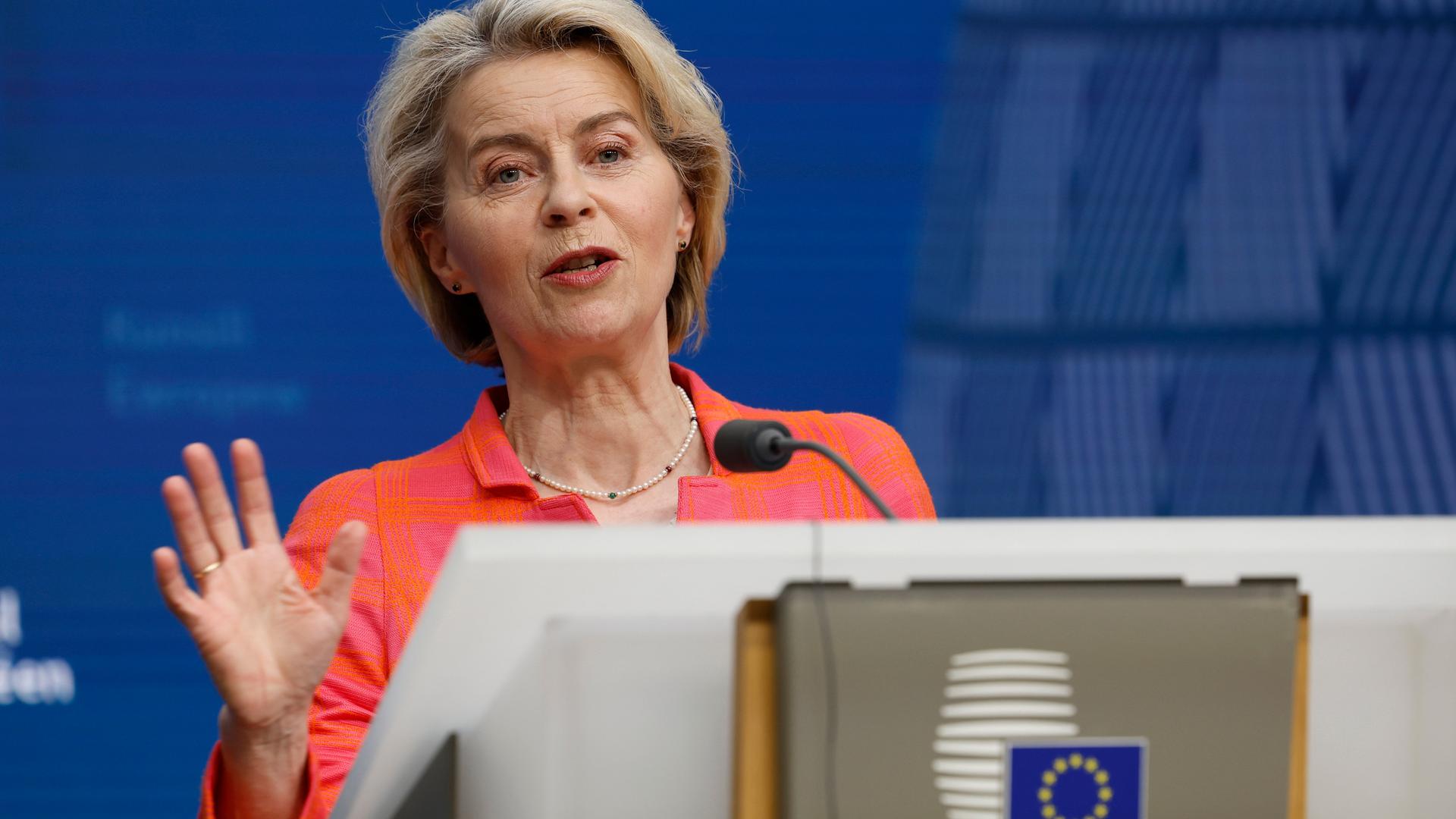 Die Präsidentin der EU-Kommission, Ursula von der Leyen (CDU) steht an einem Rednerpult und hebt ihre rechte Hand, sodass ihre Handinnenfläche sichtbar wird. 