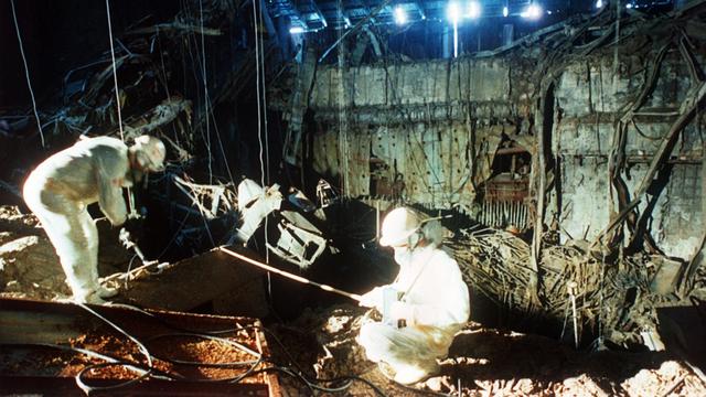 Eine historische Aufnahme von 1986 zeigt, wie zwei Helfer in weißer Schutzkleidung in den Trümmern des zerstörten Atomkraftwerks in Tschernobyl aufräumen. 