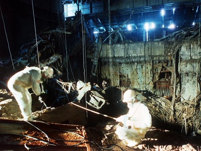 Eine historische Aufnahme von 1986 zeigt, wie zwei Helfer in weißer Schutzkleidung in den Trümmern des zerstörten Atomkraftwerks in Tschernobyl aufräumen. 